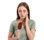 Young woman with sensitive teeth and cold ice-cream on white background