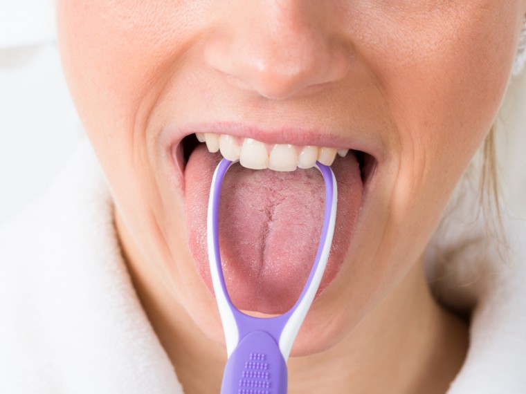Frau verwendet Zungescharber bei der Reinigung der Zunge (© Depositphotos)