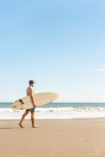 Mann mit Surfbrett am Strand neben Meer